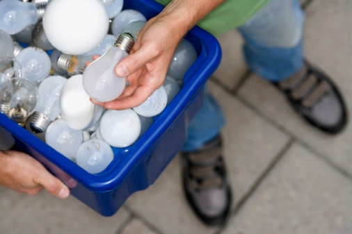 un-recipiente-con-varios-focos-de-luz-y-una-mano-sosteniendo-una-bombilla