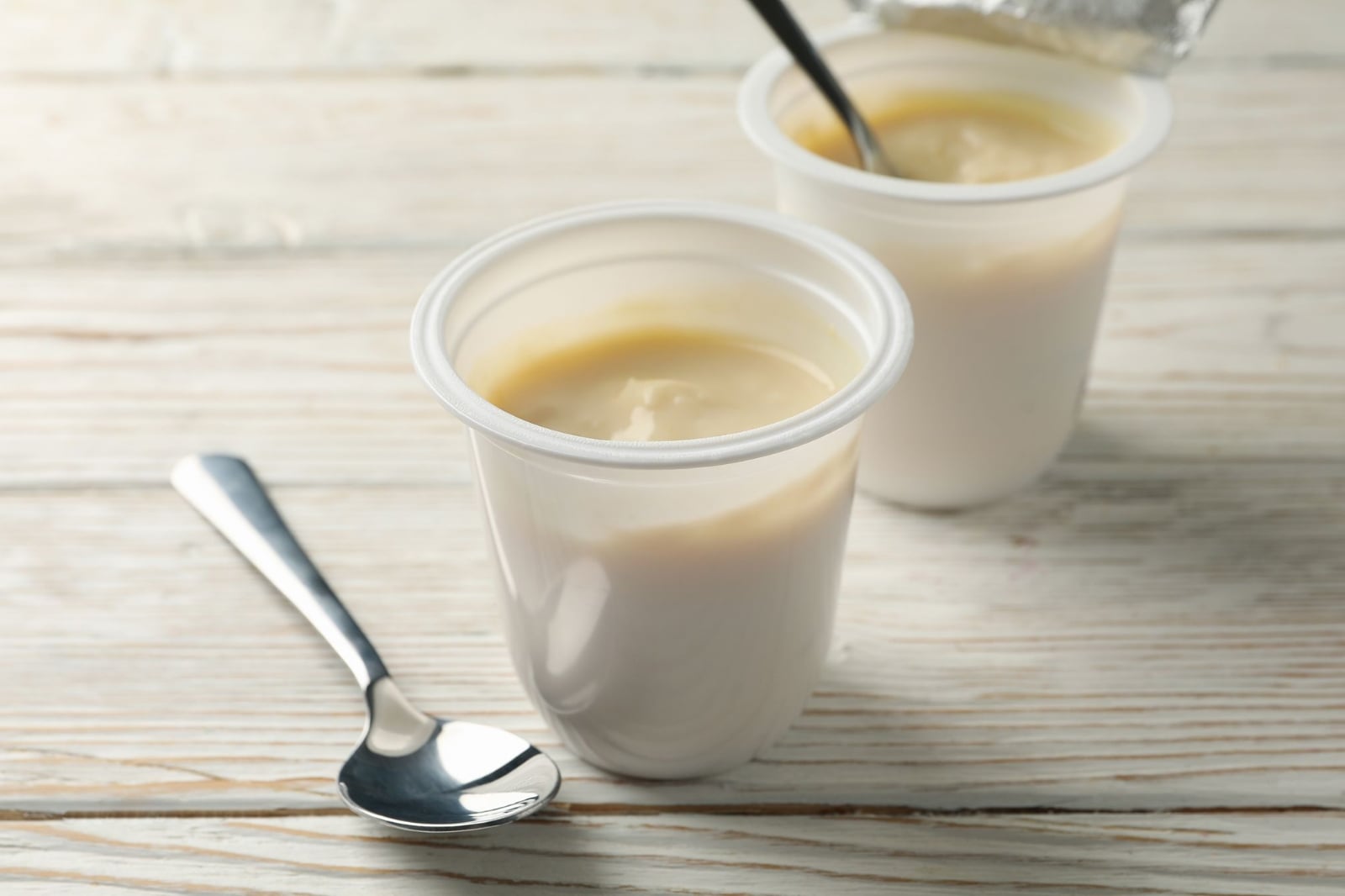 plastic-cups-of-yogurt-and-spoons-on-white-wooden-2021-08-31-14-51-49-utc