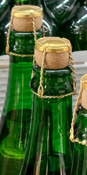 muchas-botellas-de-vidrio-champán-cerca-corchos-en-vino-concepto-producción-y-venta-alcohol-tapa-sobre-verdes-seco-166194493