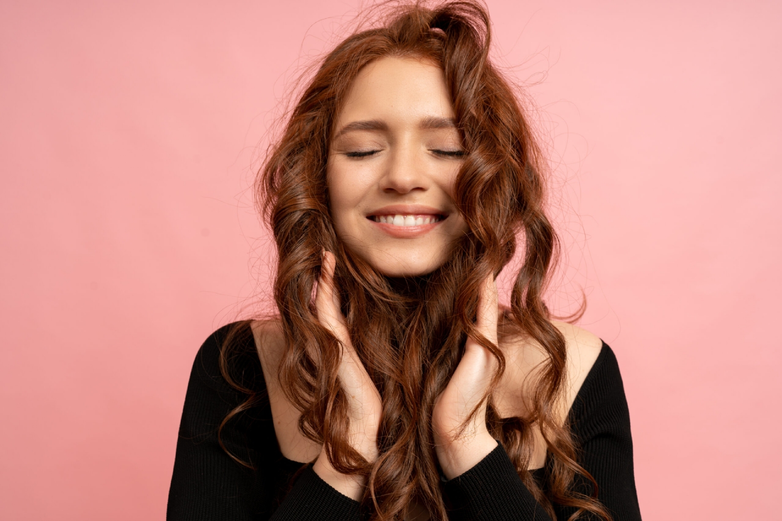 hermosa-mujer-pelirroja-ojos-cerrados-posando-sobre-pared-rosa-pelos-ondulados-sonrisa-perfecta-scaled